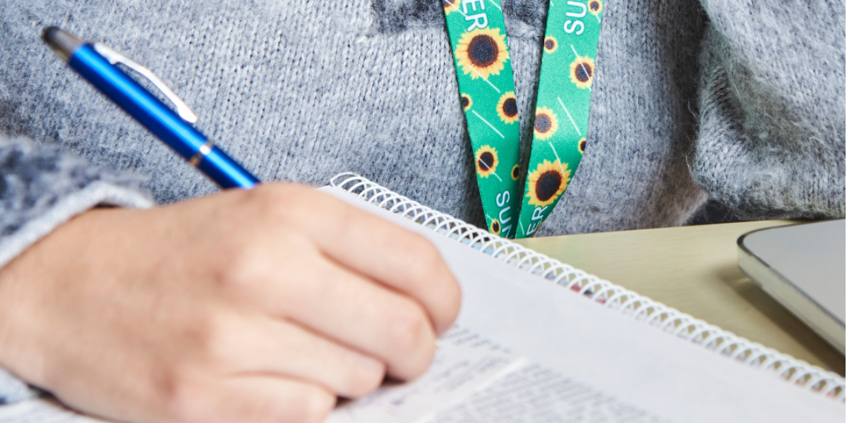 person wearing hidden disabilities sunflower lanyard and writing with blue pen on a notebook