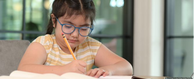 kid with learning disability writing with a pencil on a book