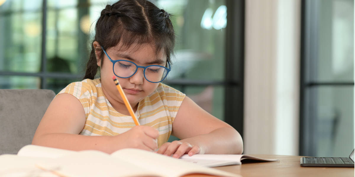kid with learning disability writing with a pencil on a book